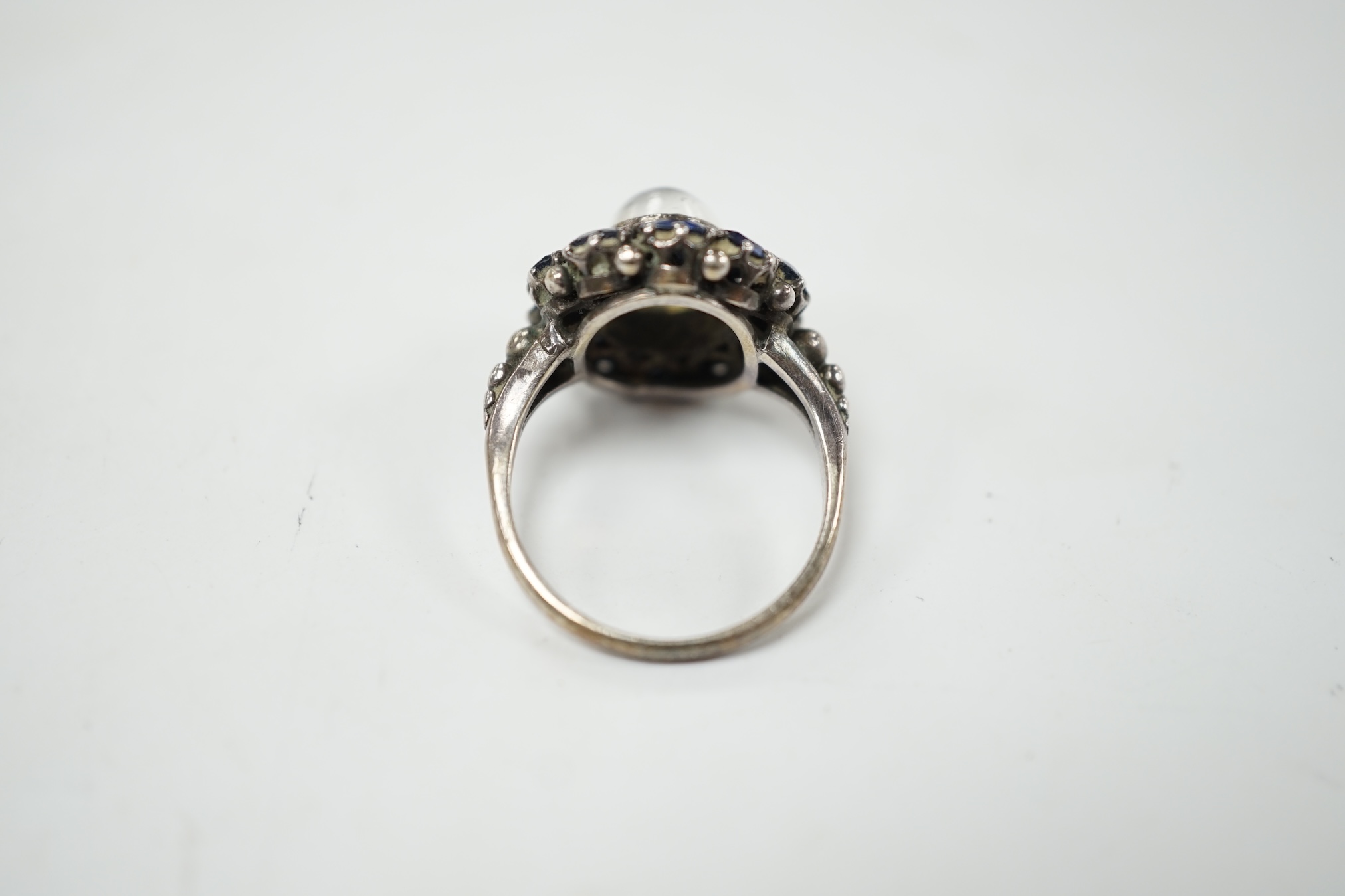 An Arts & Crafts white metal, moonstone and sapphire set circular cluster ring, in the manner of Sibyl Dunlop, size M. Condition - fair
